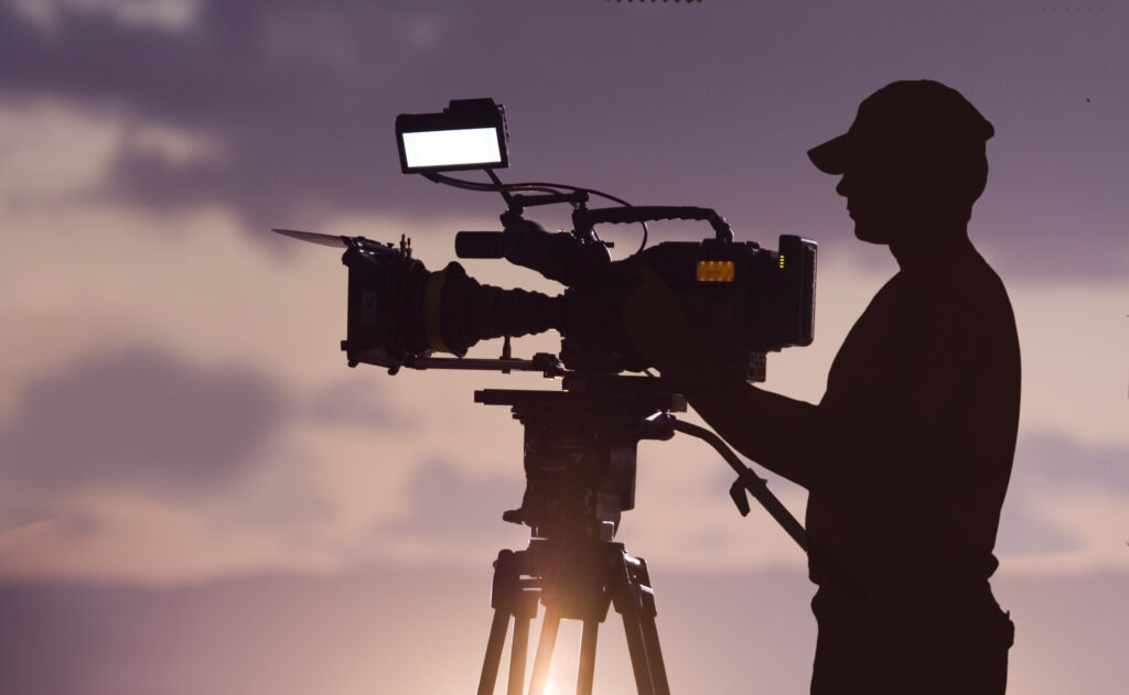 Man, outside at dusk, setting up camera to shoot a scene.